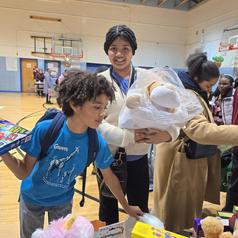 A young boy holding toys and a girl carrying stuffed animals in a gymnasium.