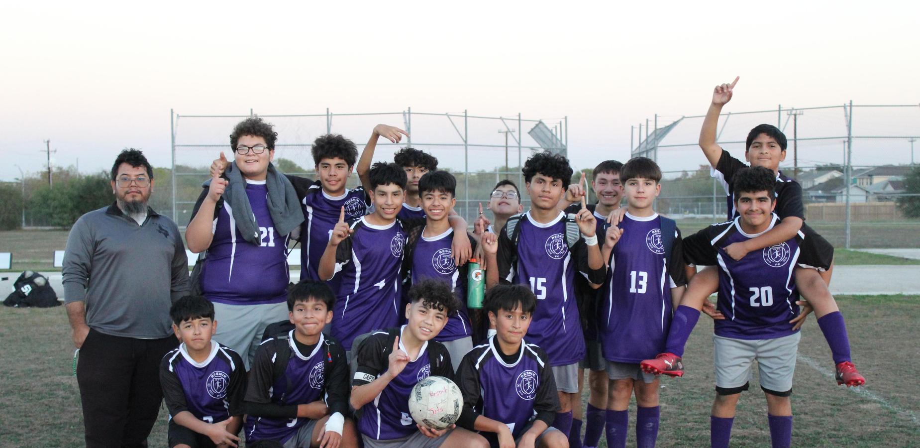 A group of young soccer players in purple uniforms posing together on a field.