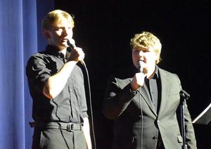 One young man sings into a microphone while another listens attentively.