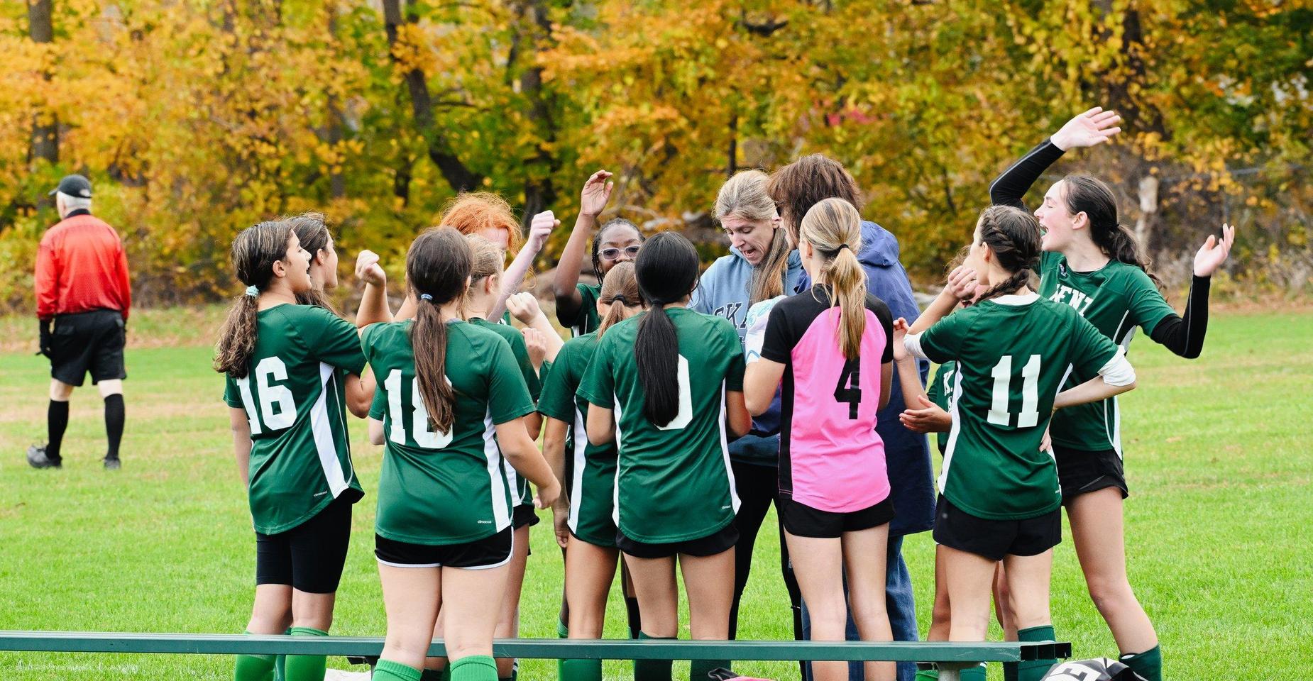A group of female soccer players huddle together with a coach on a green field.
