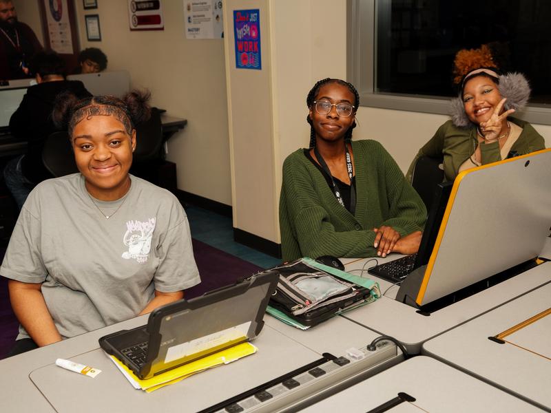 Three female students smiling at the camera in class.