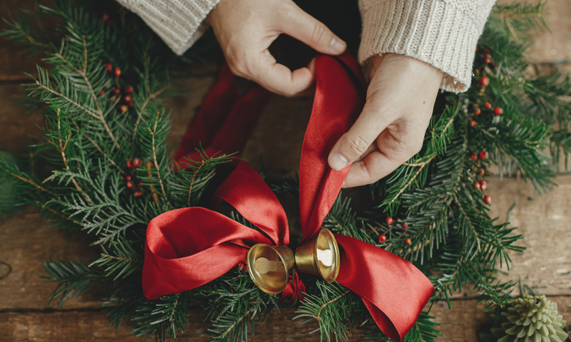 Close up of hands tying a red bow on an evergreen wreath