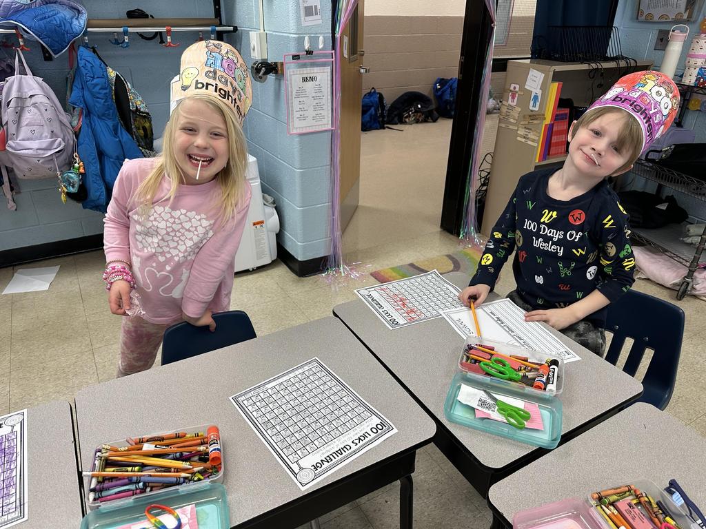 Two students smiling with lollipops in their mouths.