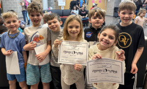 A team of smiling students at the Odyssey of the Mind competition holding up certificates.