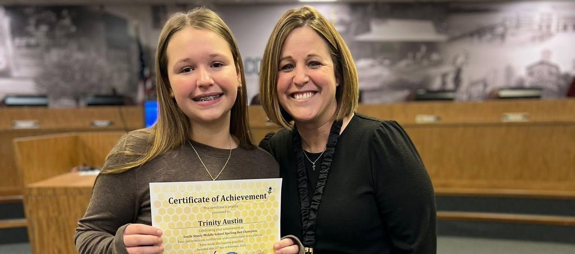 Two individuals holding a Certificate of Achievement in a classroom setting.