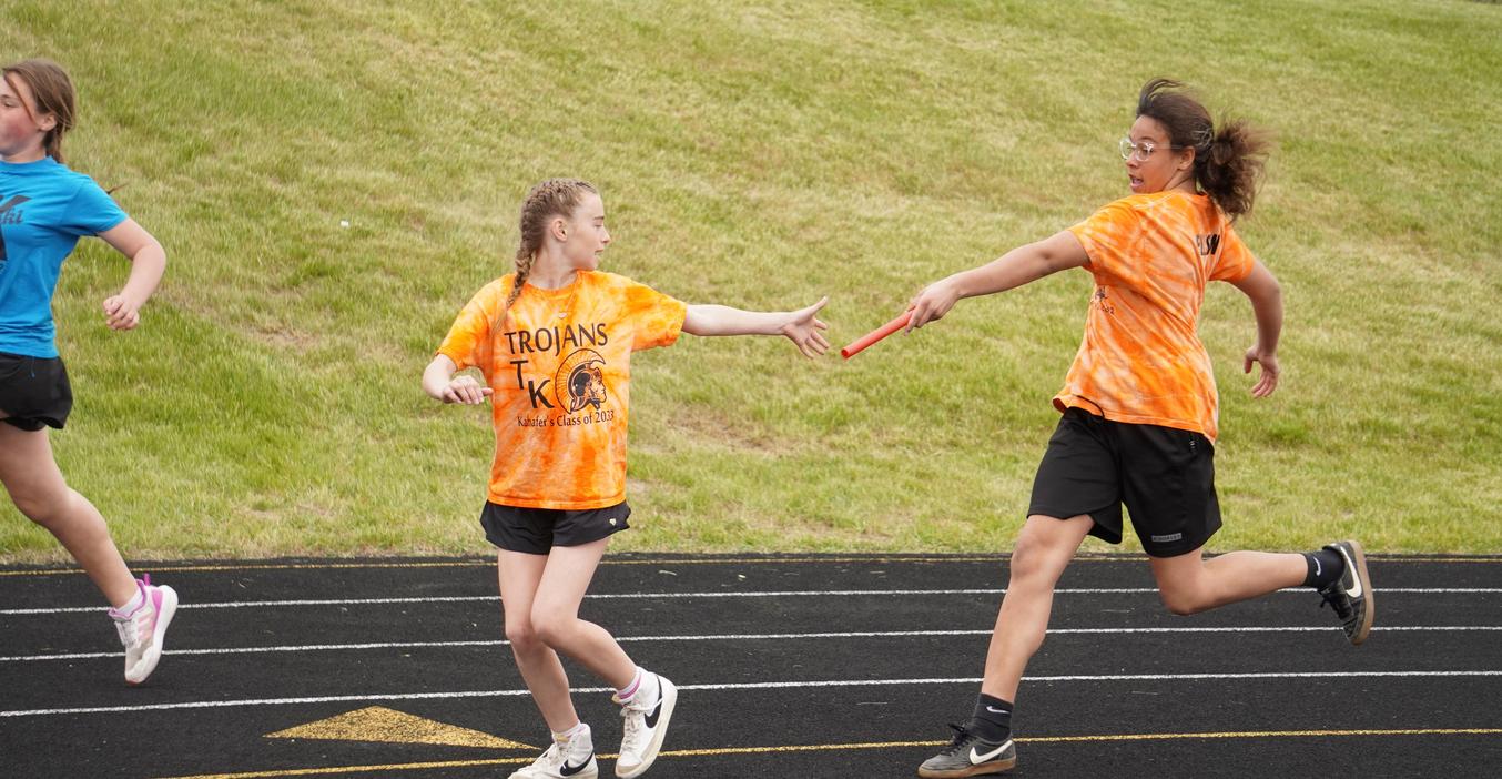 Two girls participate in a relay race, passing a baton on a track.