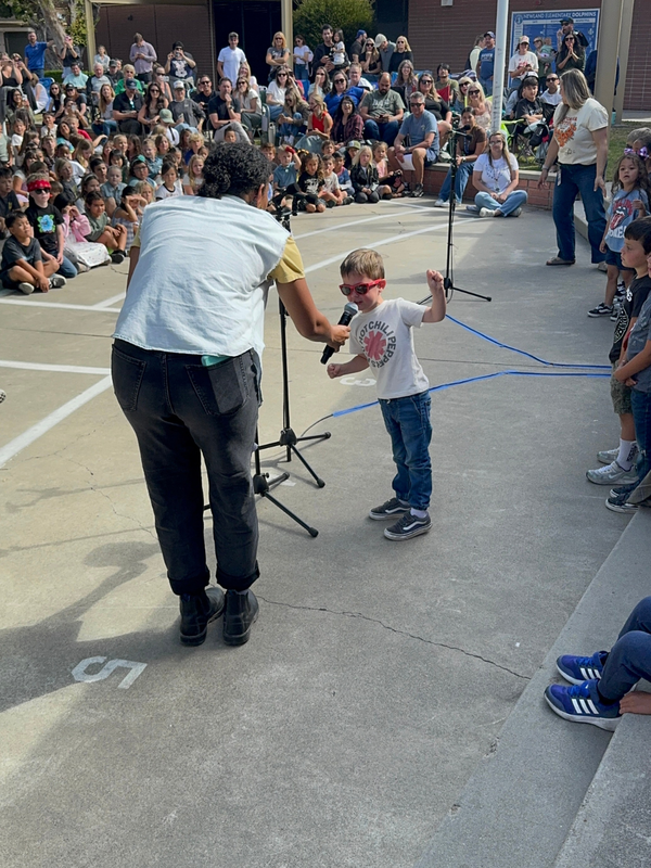 A child wearing sunglasses performs on stage in front of an audience.