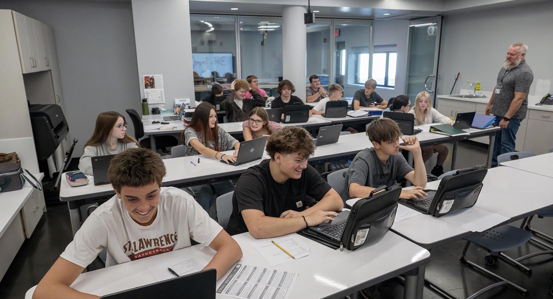 High school students smile while working on laptops.