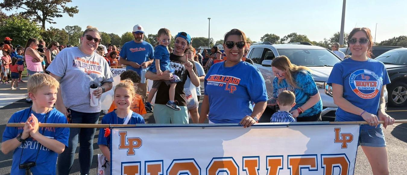 Hoover staff and students smile while holding a large white and orange "HOOVER" school banner.