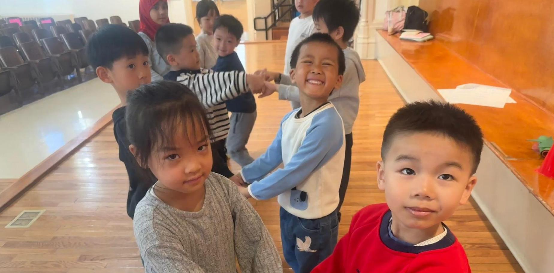 Children holding hands and smiling in a classroom setting.