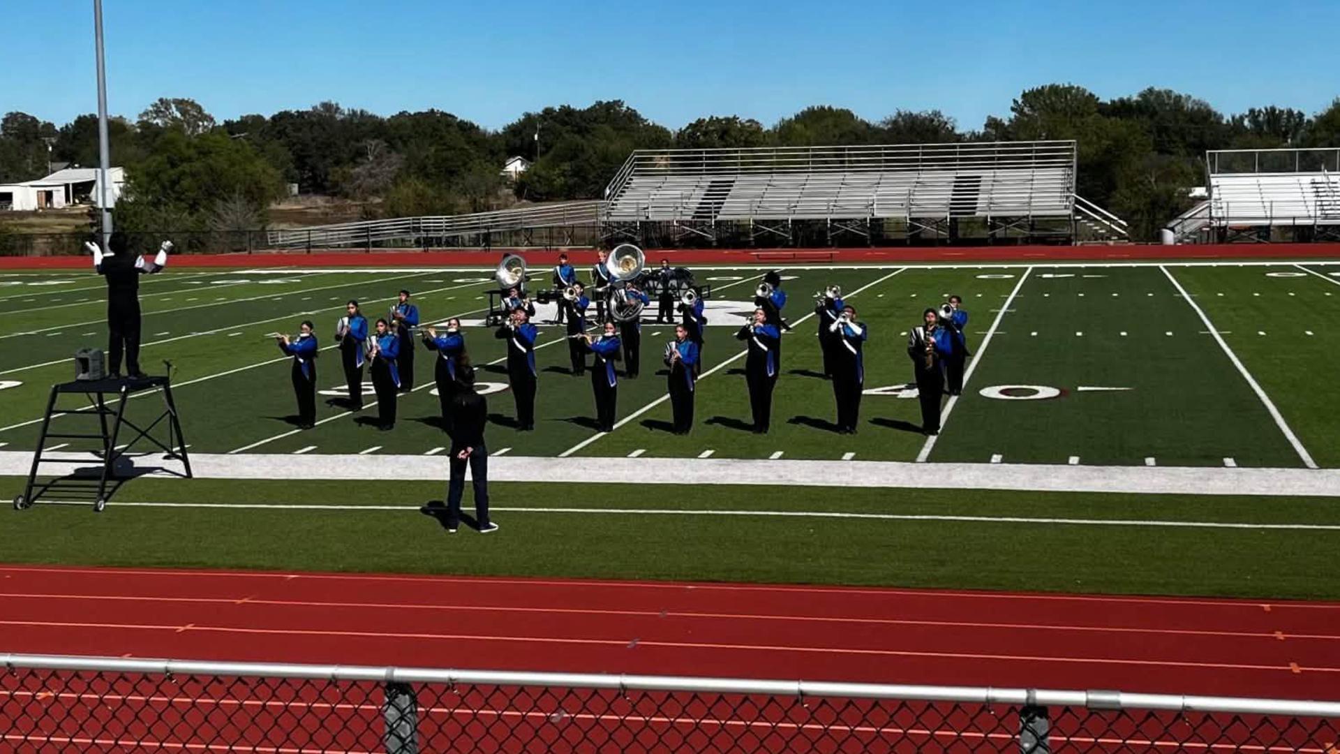 A marching band performing on a football field under a clear blue sky.