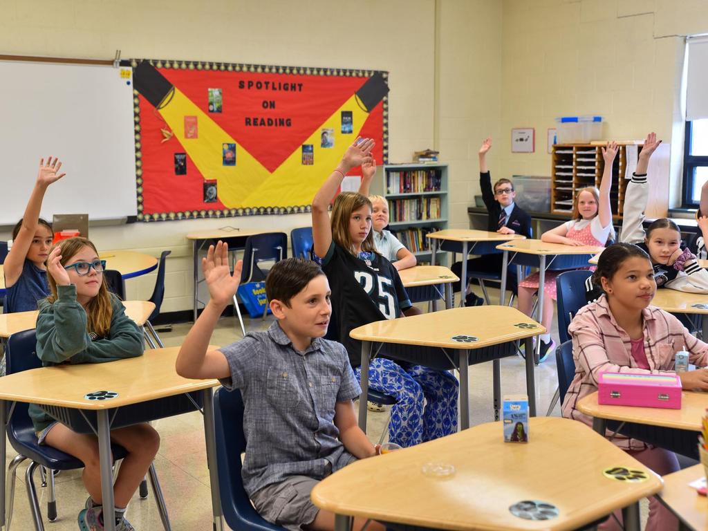 Students raising their hands in a classroom.