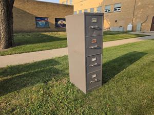A single gray file cabinet placed on grass near a building