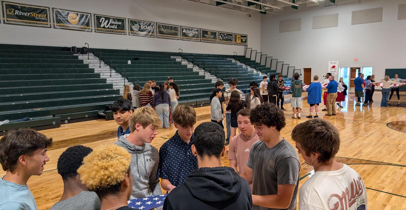 Groups of students gather around to participate in an activity involving a flag.