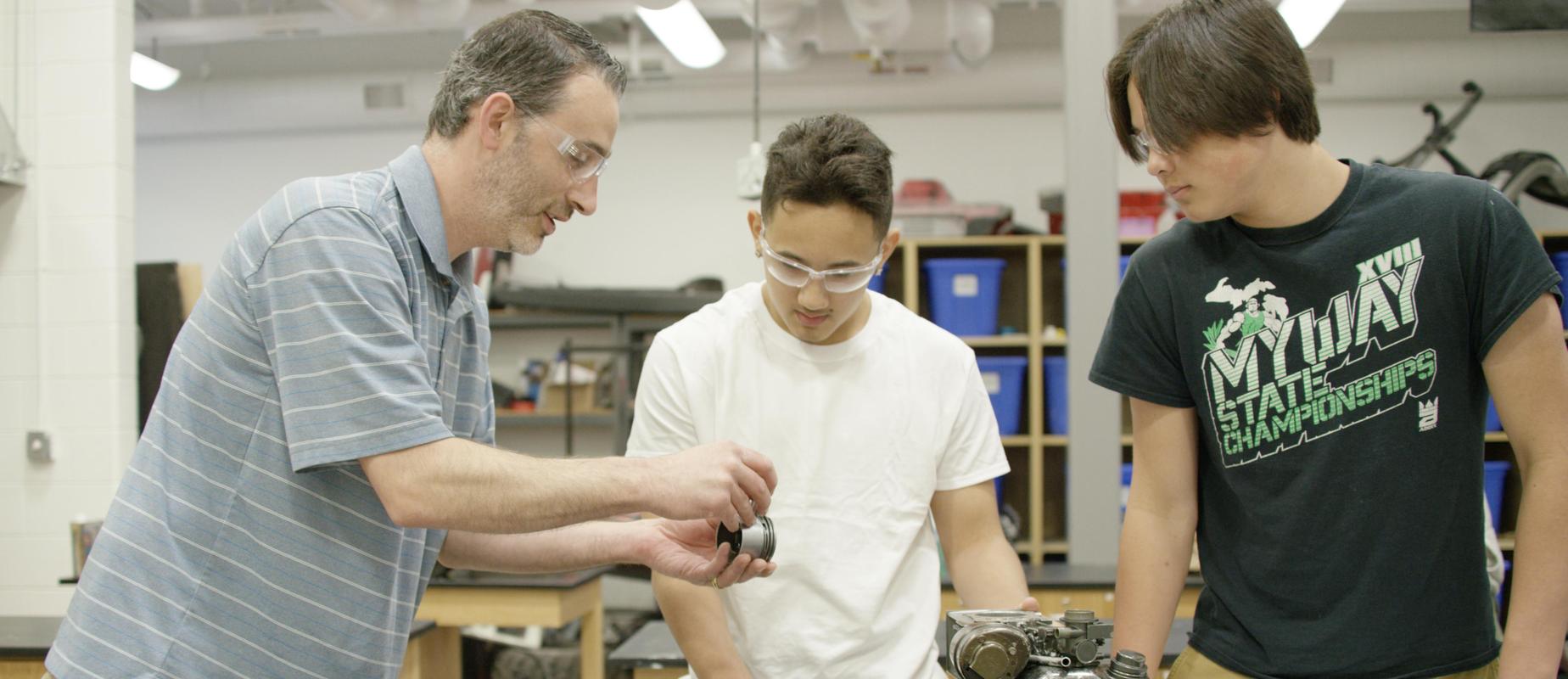 teacher shows two high school boys a machine part