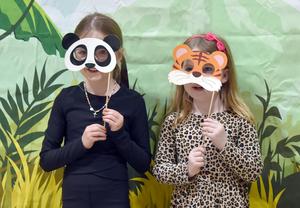 Two girls wear animal masks, posing in front of a jungle backdrop.