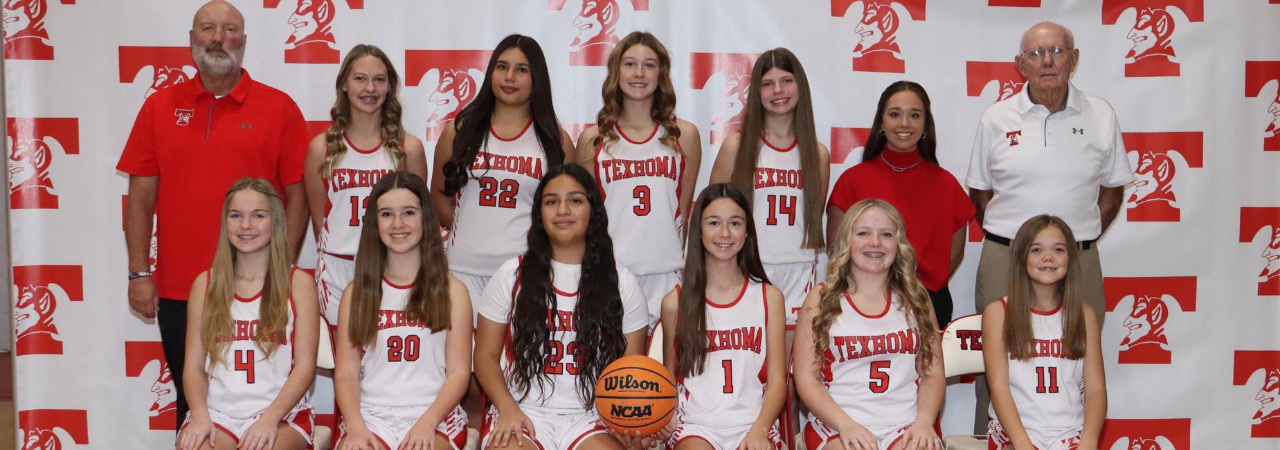 Girls basketball team posed together in uniforms with a basketball at the front.