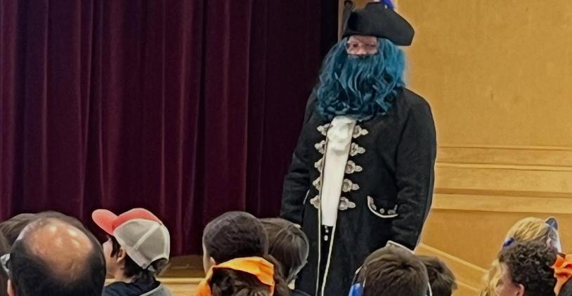 A performer in a pirate costume with a blue beard standing before an audience.