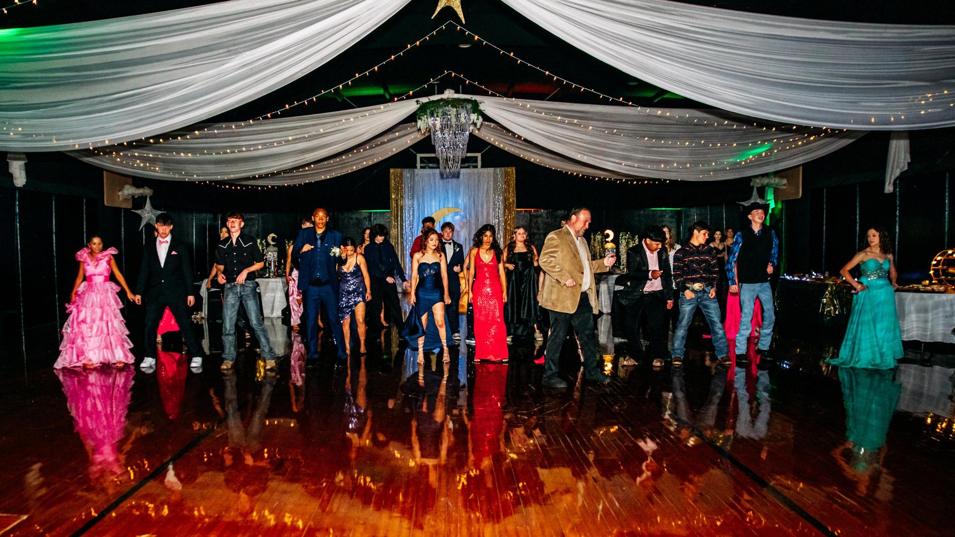 A group of people dancing at prom event with twinkling lights.