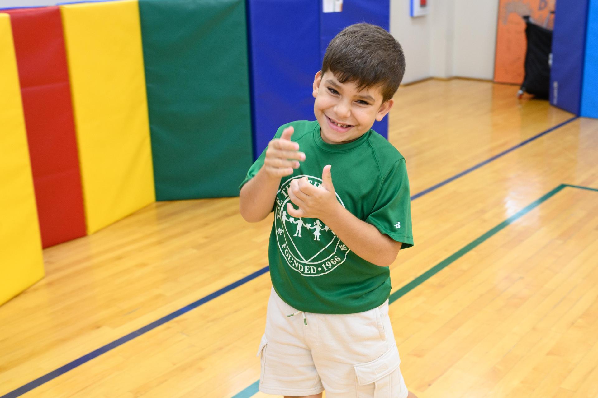 Young student in green shirt with thumbs up in gym