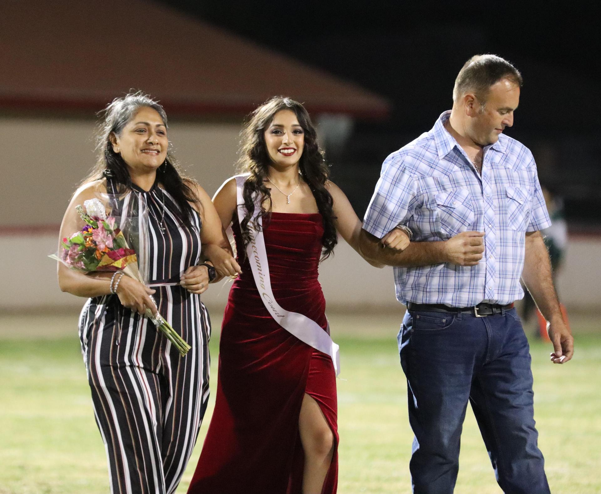 homecoming king and queen candidates walking across the field with their escorts