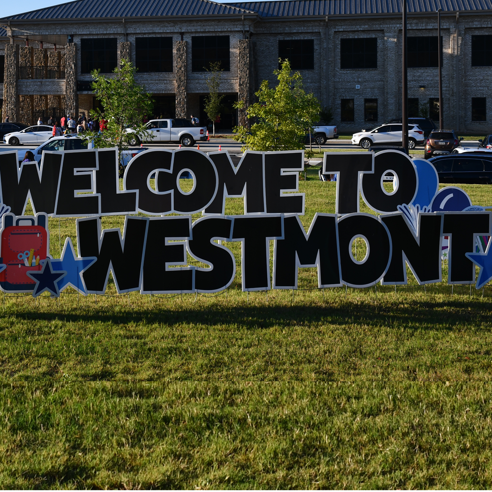 Large colorful welcome sign to Westmont, with a building and parked cars in the background.