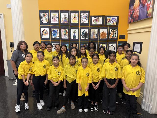 Group of chorus students in yellow shirts posing in front of a mural display.