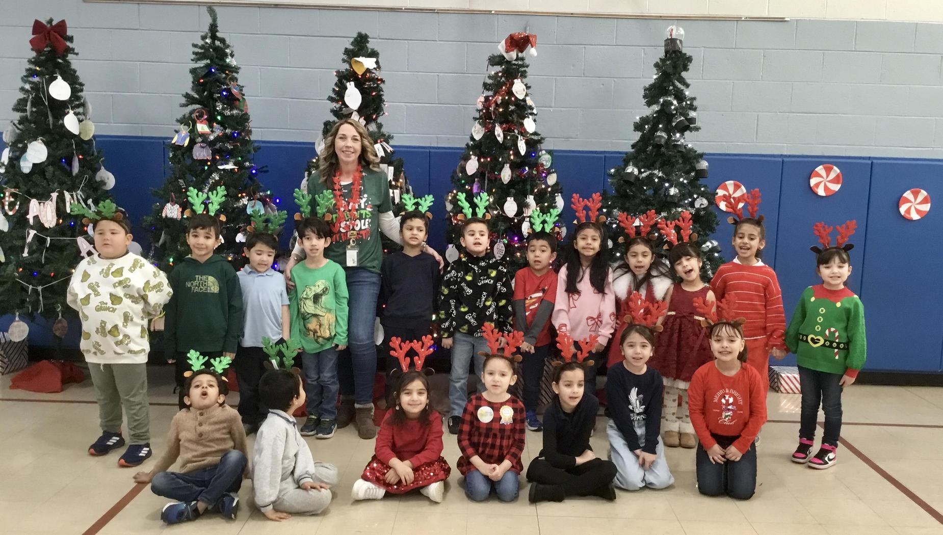 A group of children in festive attire posing in front of decorated Christmas trees.
