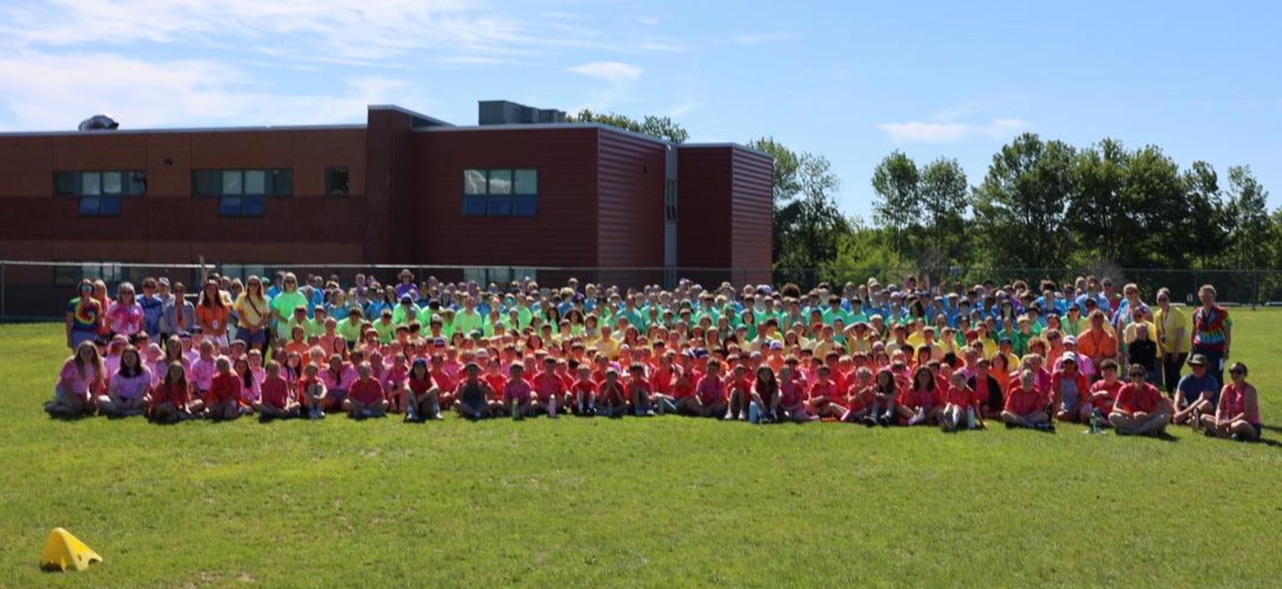 A large group of students in colorful shirts gathered on a grassy field.