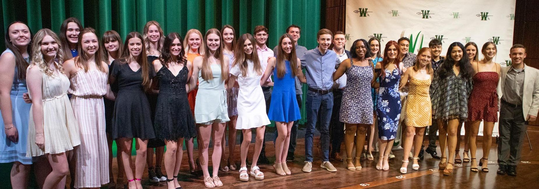 group of 24 girls & 6 boys pose together on stage