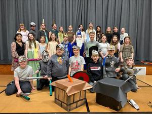 A large group of students in costumes poses together on stage after a performance.