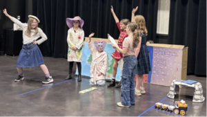 A team of elementary students performing on stage in costume A team of elementary students in red headbands posing with certificates at the Odyssey of the Mind competition.