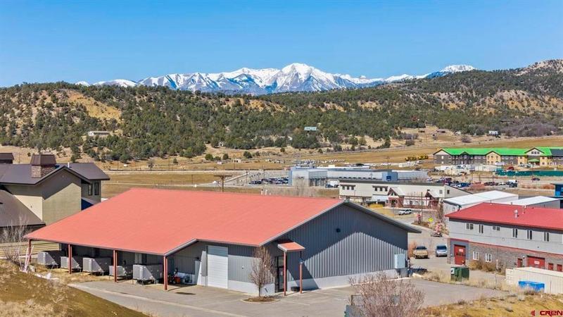 A warehouse with a red roof amidst an industrial park, with mountains in the distance