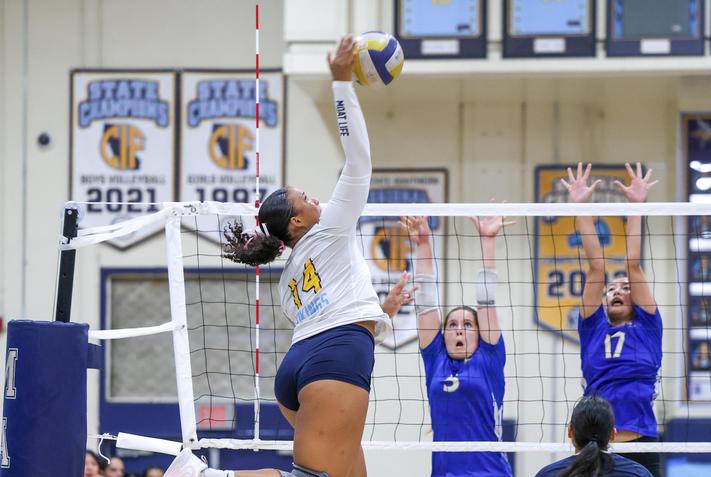MHS volleyball player hitting the ball against 2 blockers
