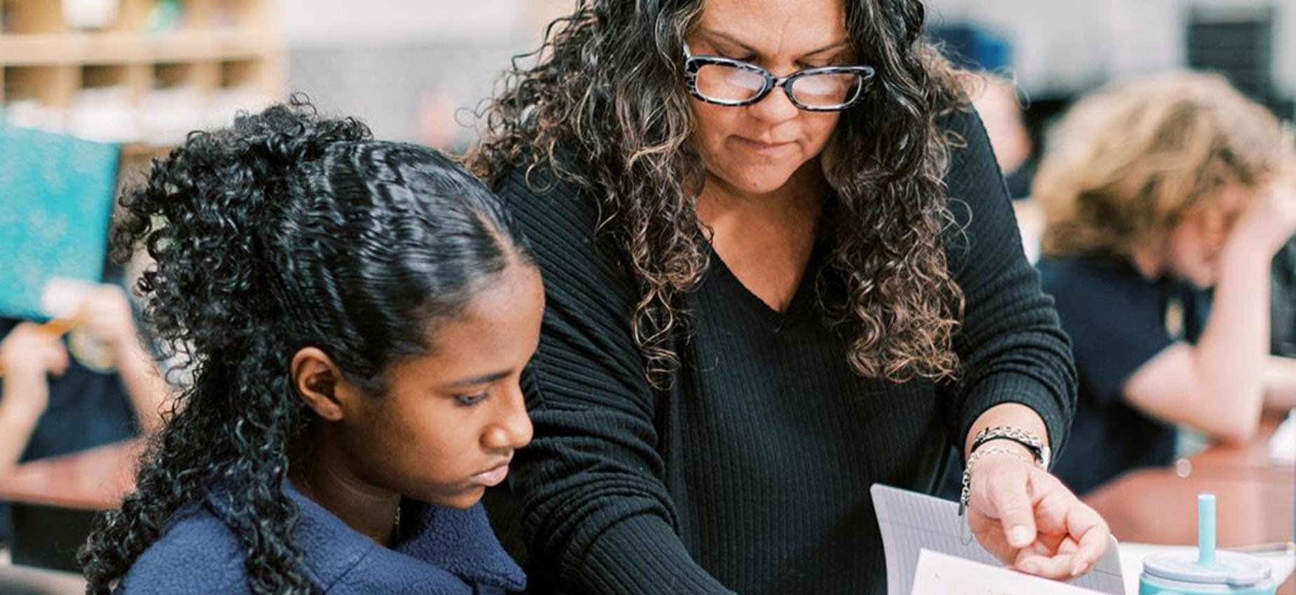 Teacher helps a student with her work at a classroom table
