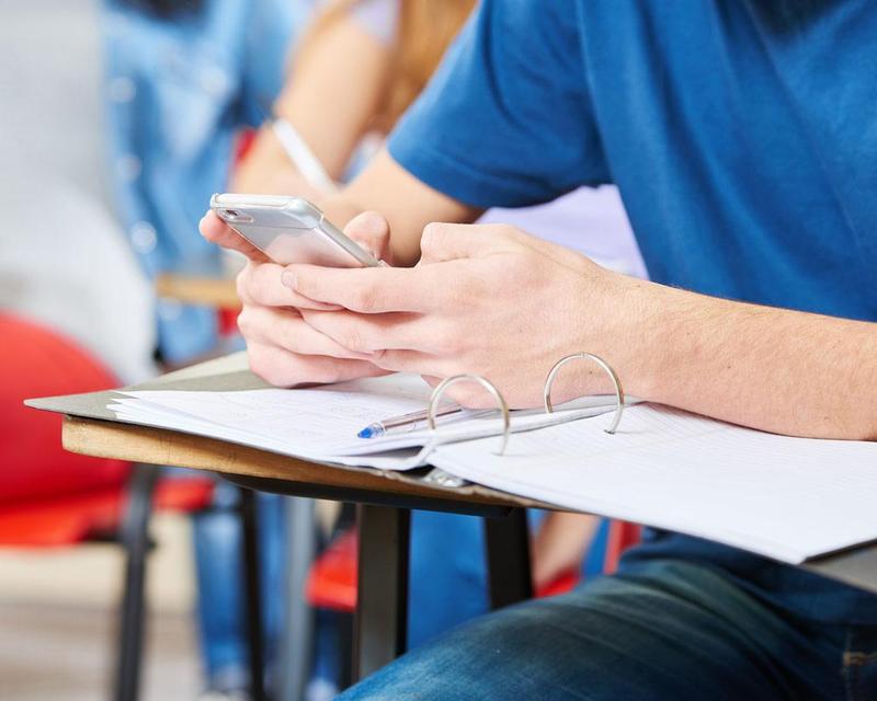 Student arms on desk with cell phone in hand