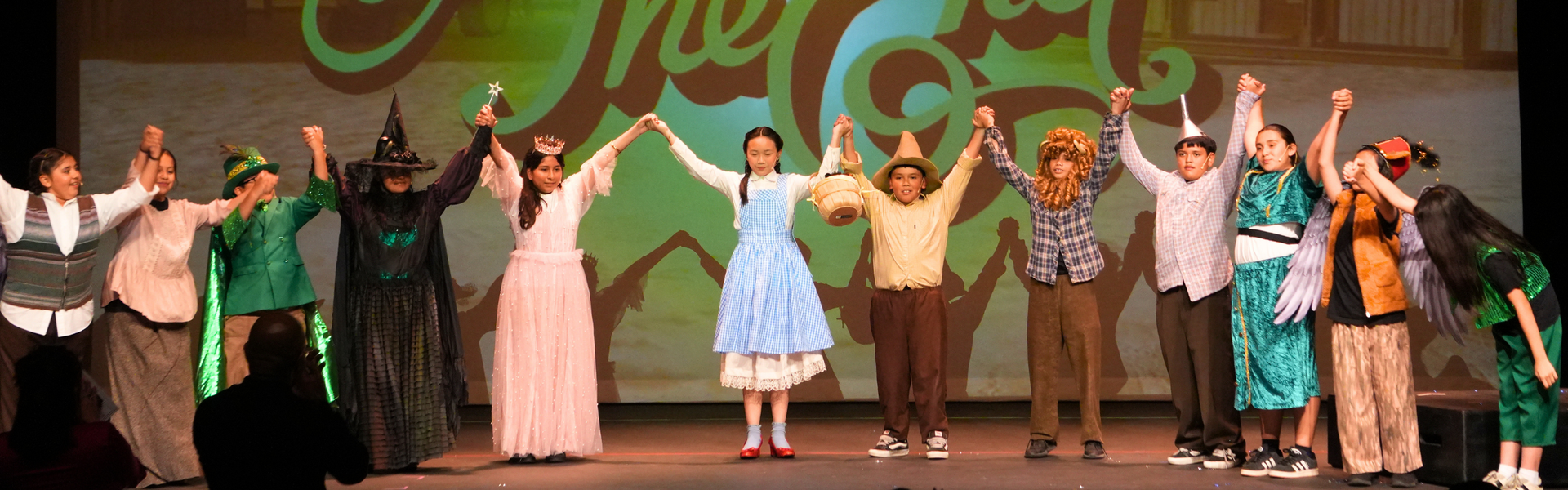Cast members perform a musical, holding hands and posing on stage.