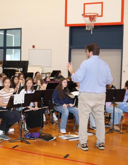 A band rehearsal with students playing various instruments in a gymnasium.