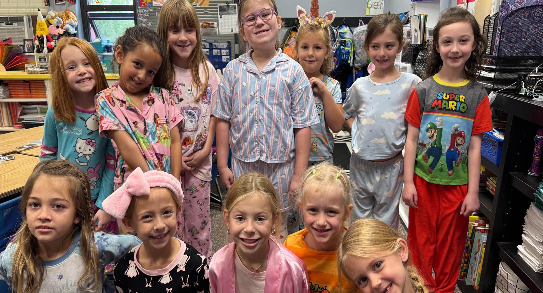 A group of girls in pajamas smiling in a classroom setting.