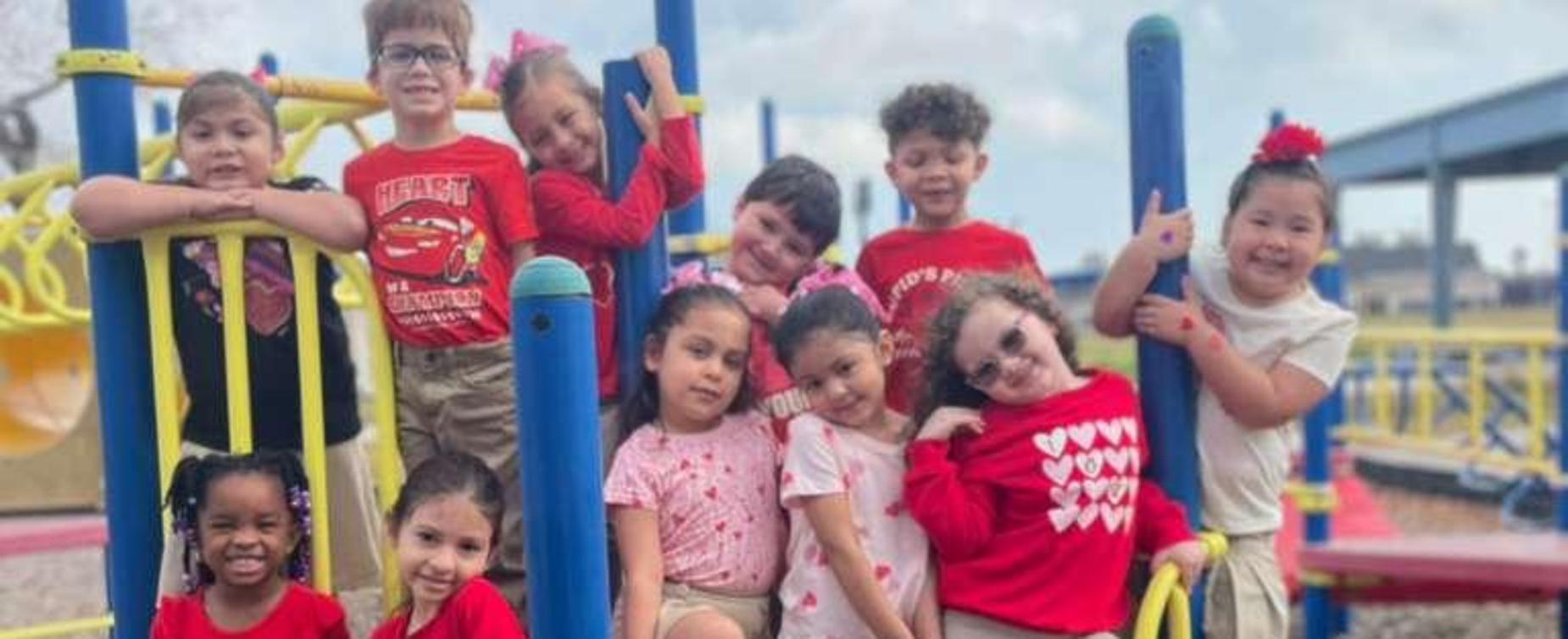 Group of children playing on a colorful playground dressed in red and white.