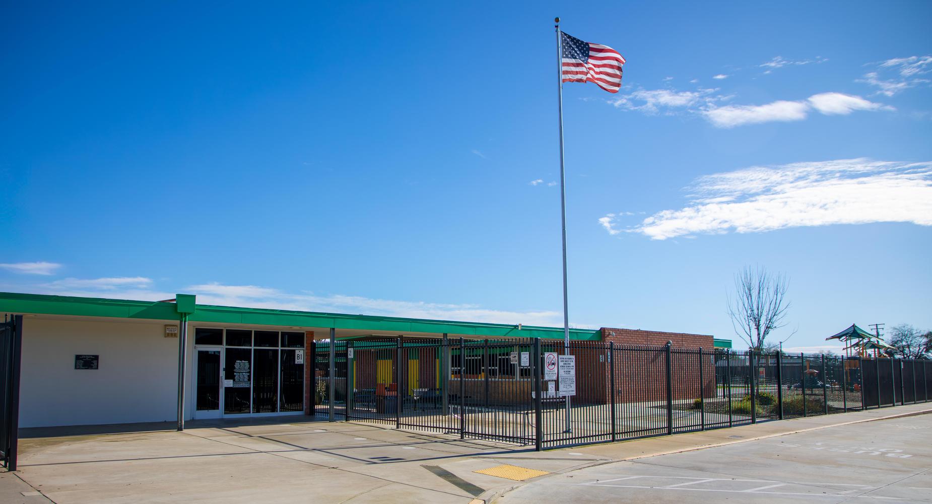Exterior view of a school building with a flag pole and clear blue sky.