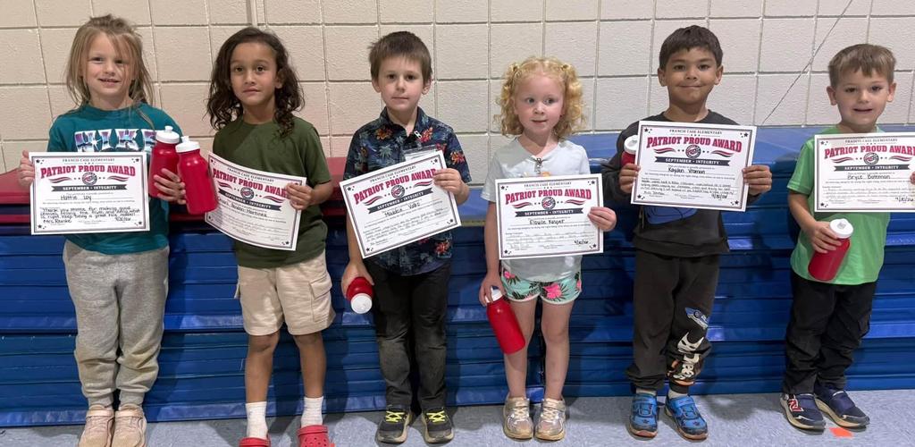 Six children holding certificates, standing in a line against a gym backdrop.