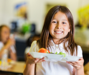 Elementary student holding a lunch tray with an apple