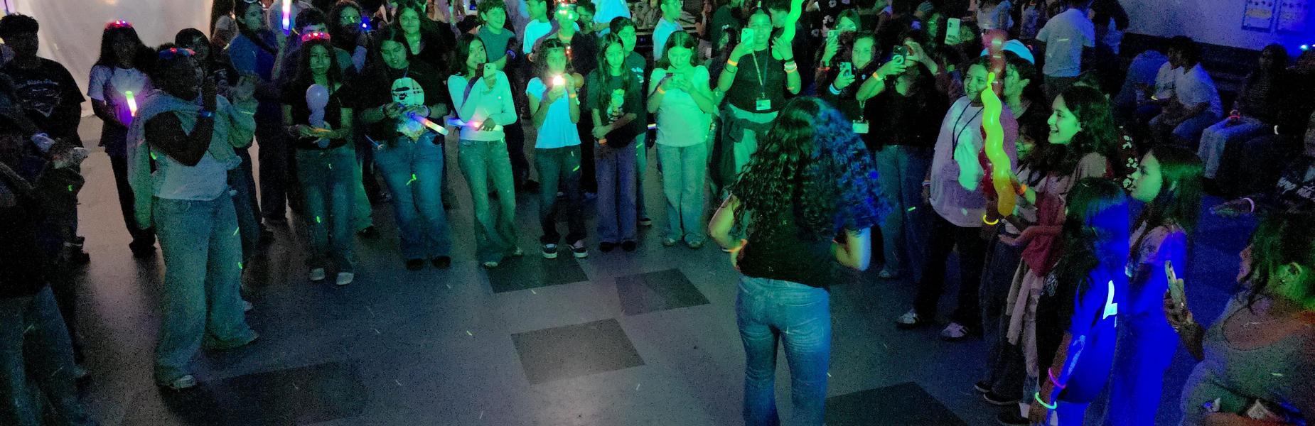 A large group of people holds glow sticks in a vibrant, energetic atmosphere.