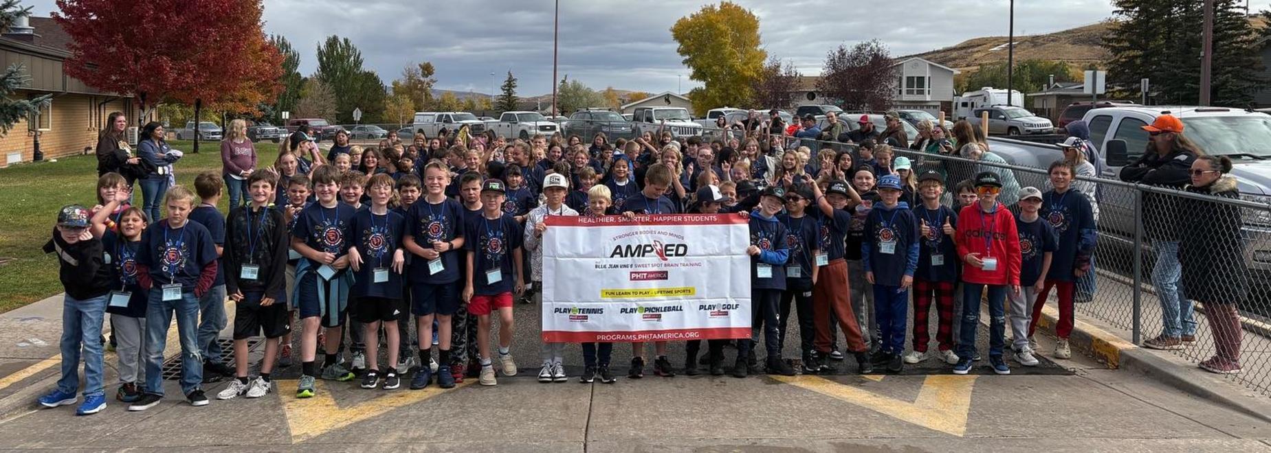 A large group of students in matching shirts holding a banner in an outdoor setting.