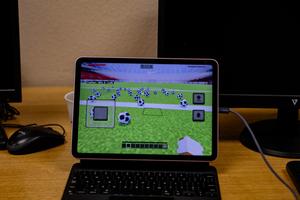 A tablet shows a Minecraft game scene with numerous soccer balls on the field.