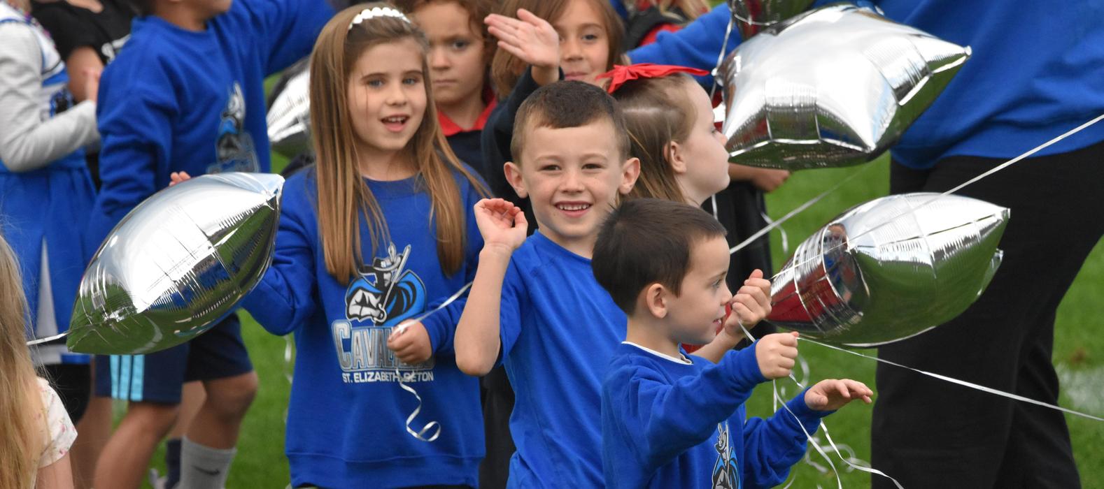 Children holding silver balloons and smiling during an outdoor event on a sunny day.