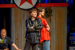 Two main leads in Godspell posing on stage with their backs to each other.