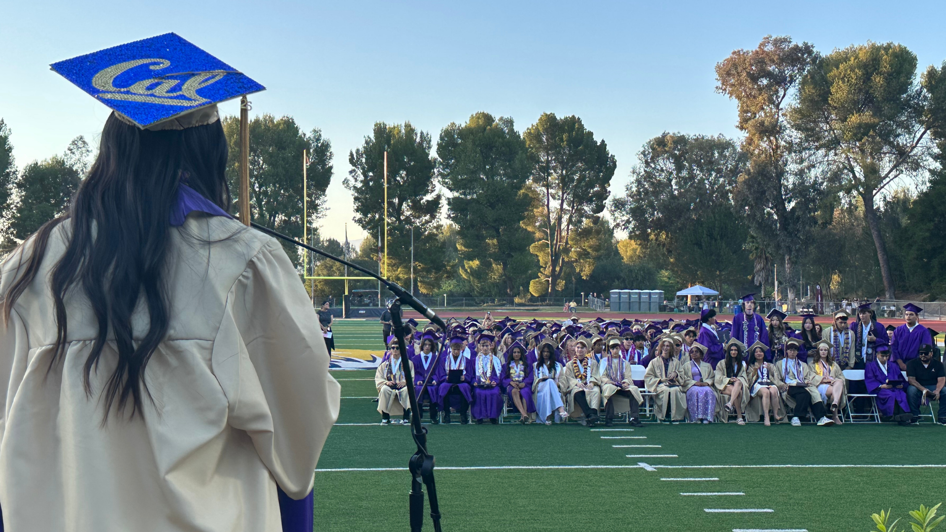 Graduation ceremony with a speaker in cap and gown addressing seated graduates.