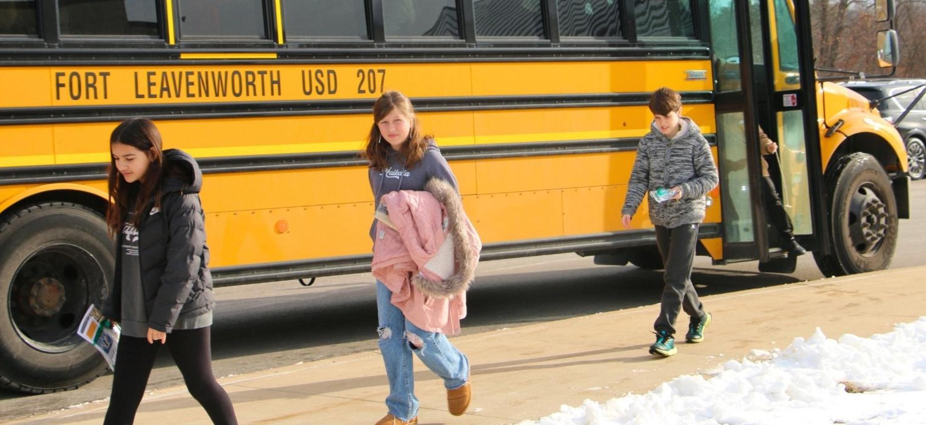 Students walking by a school bus in winter attire.